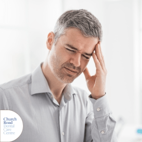 A man wearing a grey shirt resting his head in one hand and with his eyes closed